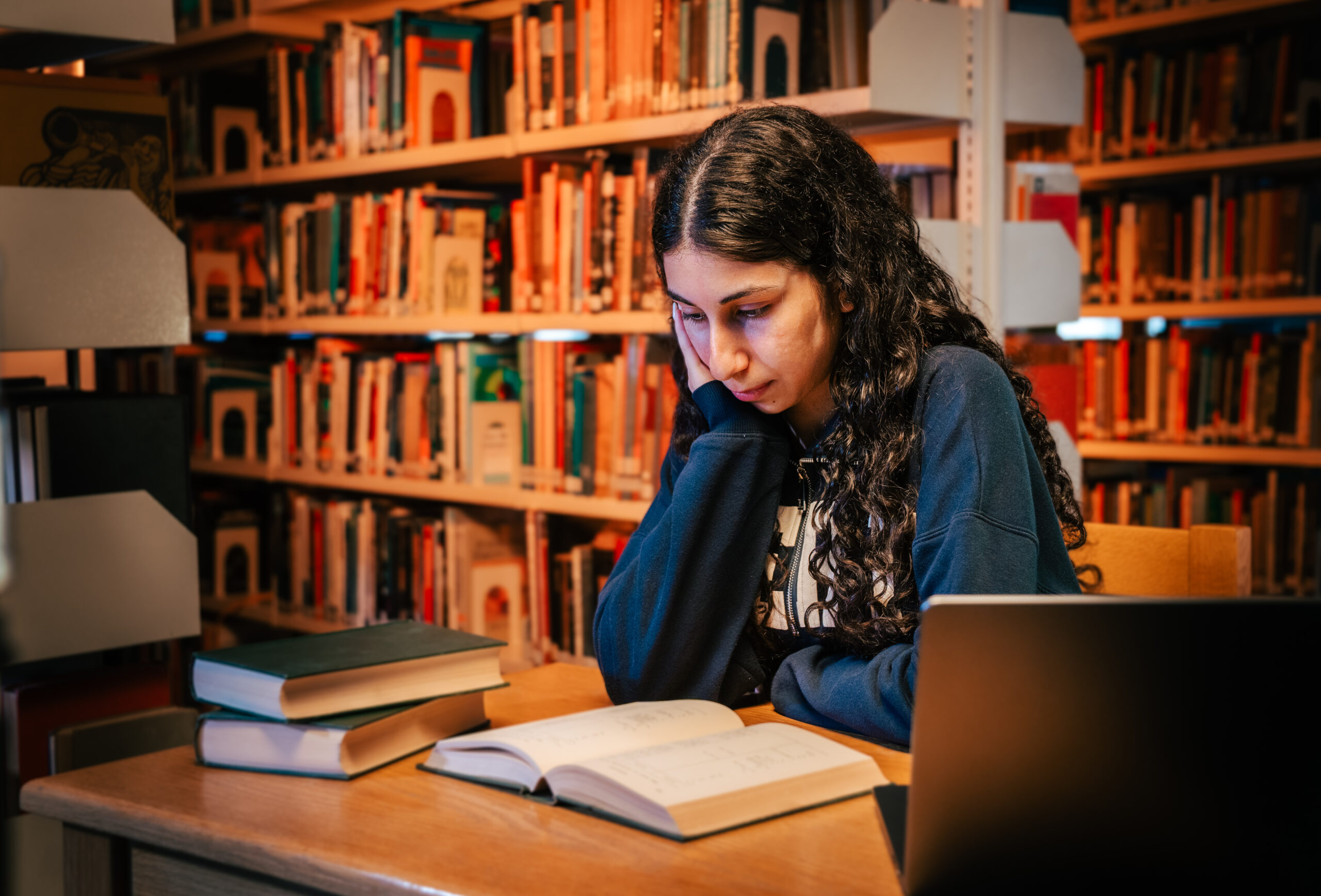 MEU student studying with books and a laptop in the university library
