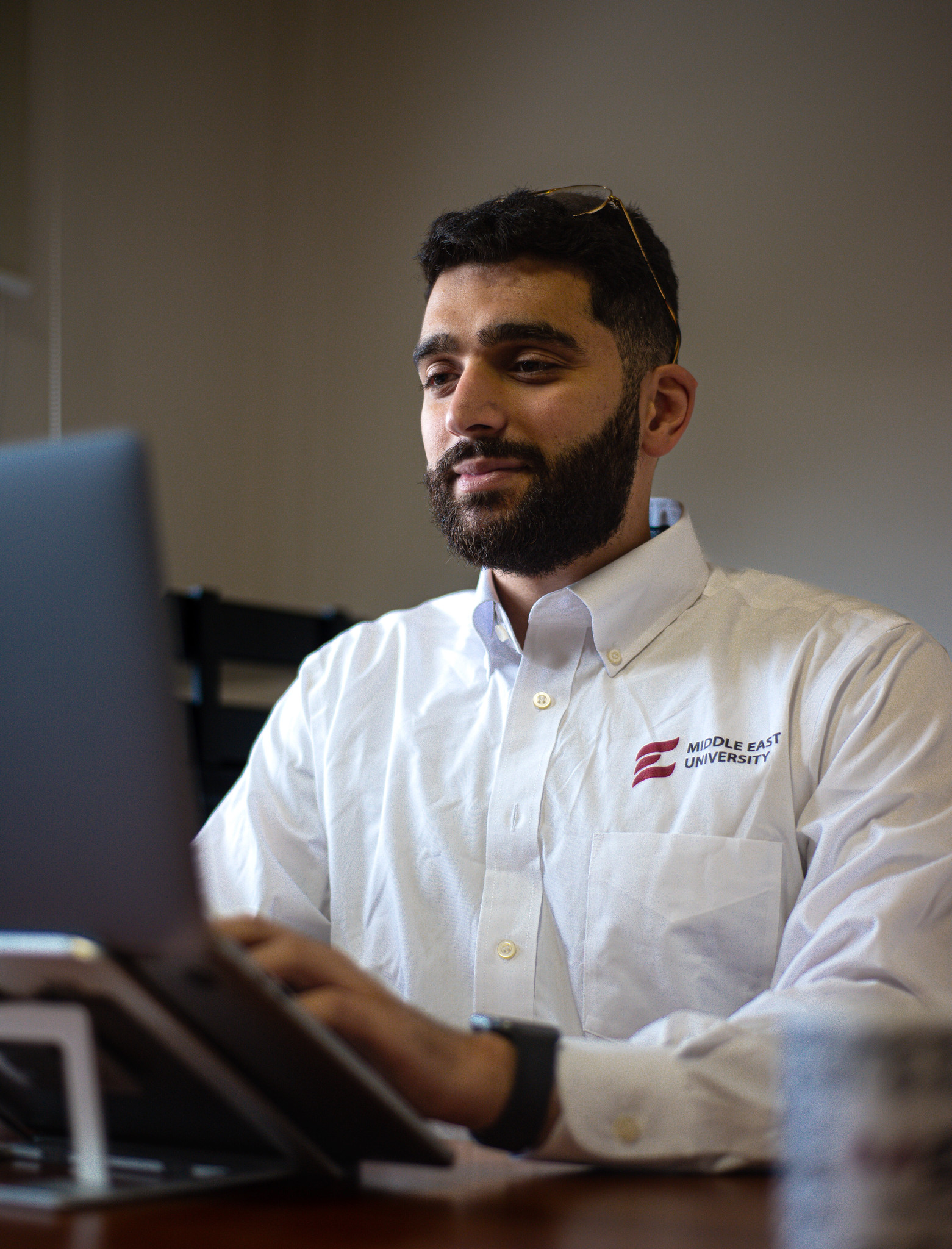 A person wearing a Middle East University shirt working at a computer in an office-like setting