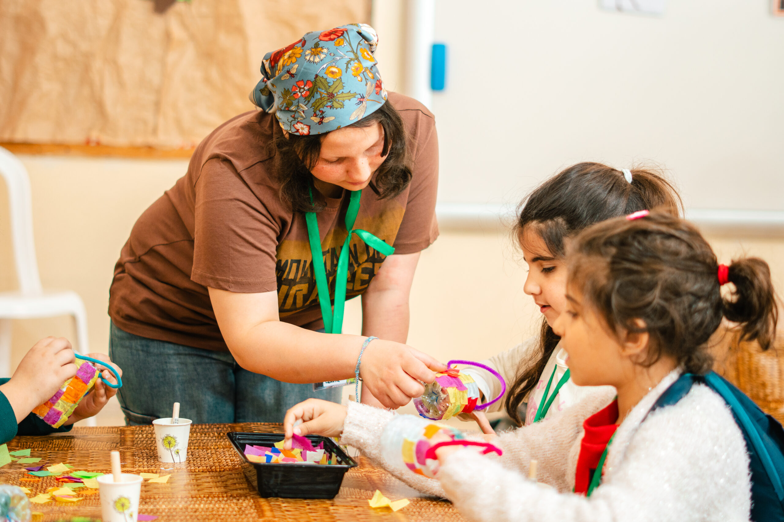 Adult helping children create colourful craft projects around a learning table