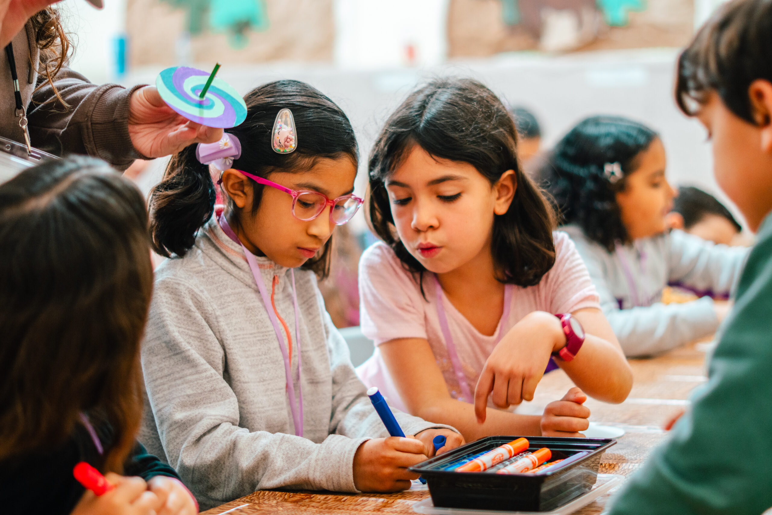 Two children collaborating on a creative learning activity with an adult nearby