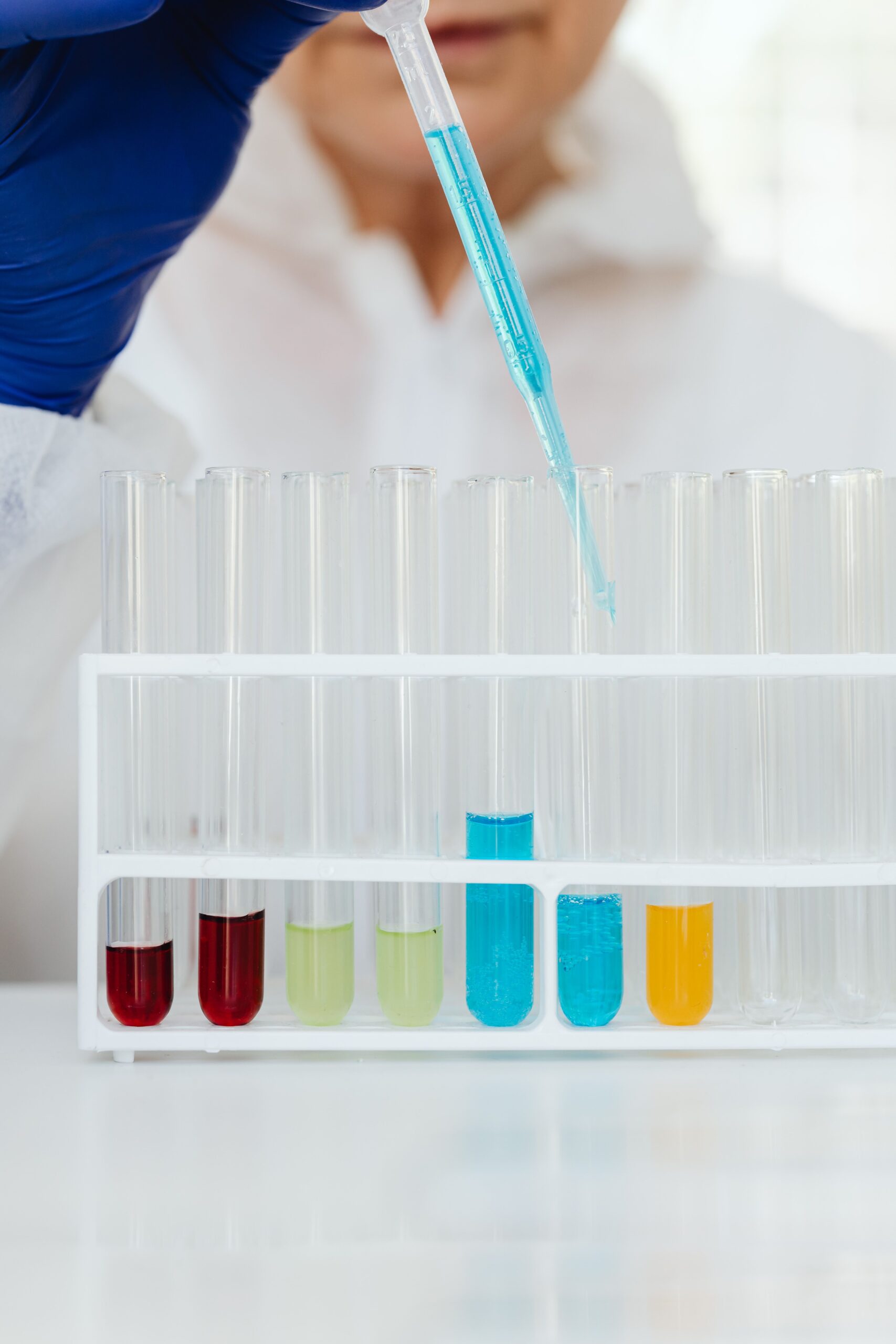 Gloved researcher using a pipette above a rack of colorful laboratory test tubes